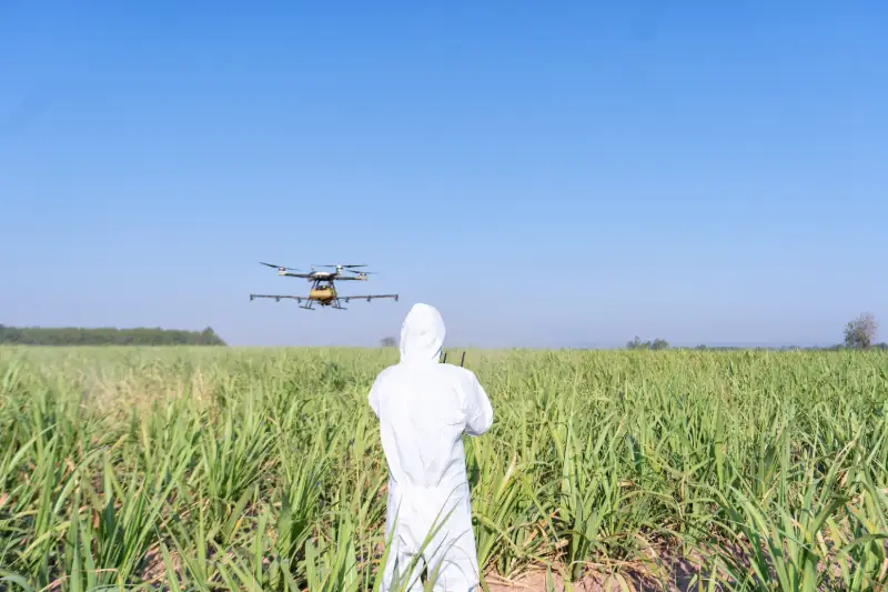 Operador agrícola com roupa de proteção controlando drone para pulverização com foco em segurança e economia de agroquímicos